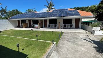A house with a solar panel roof, a covered patio area, and a well-maintained lawn.