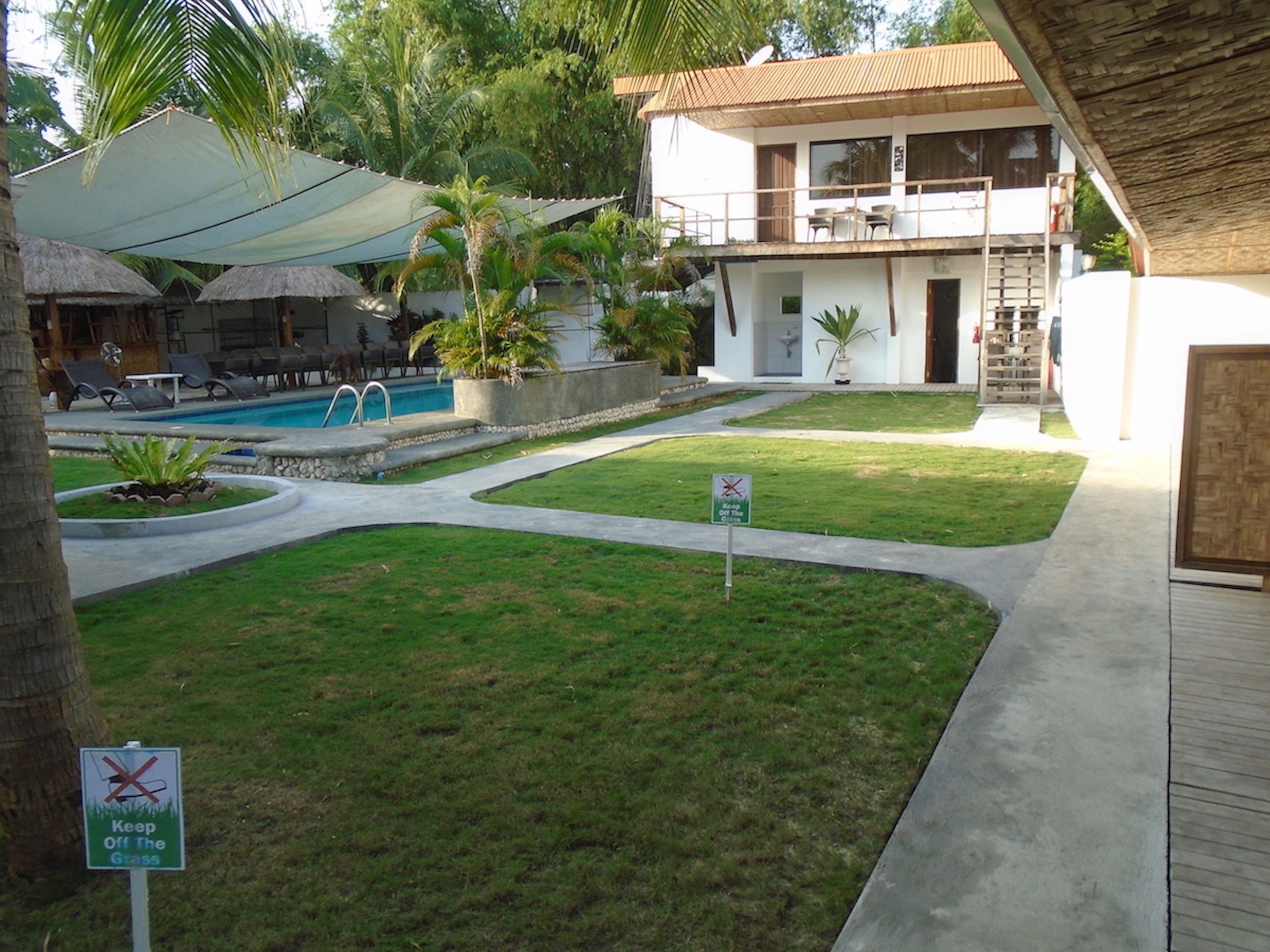 A pool area with lounge chairs and a sign indicating 'Keep Off The Grass'.