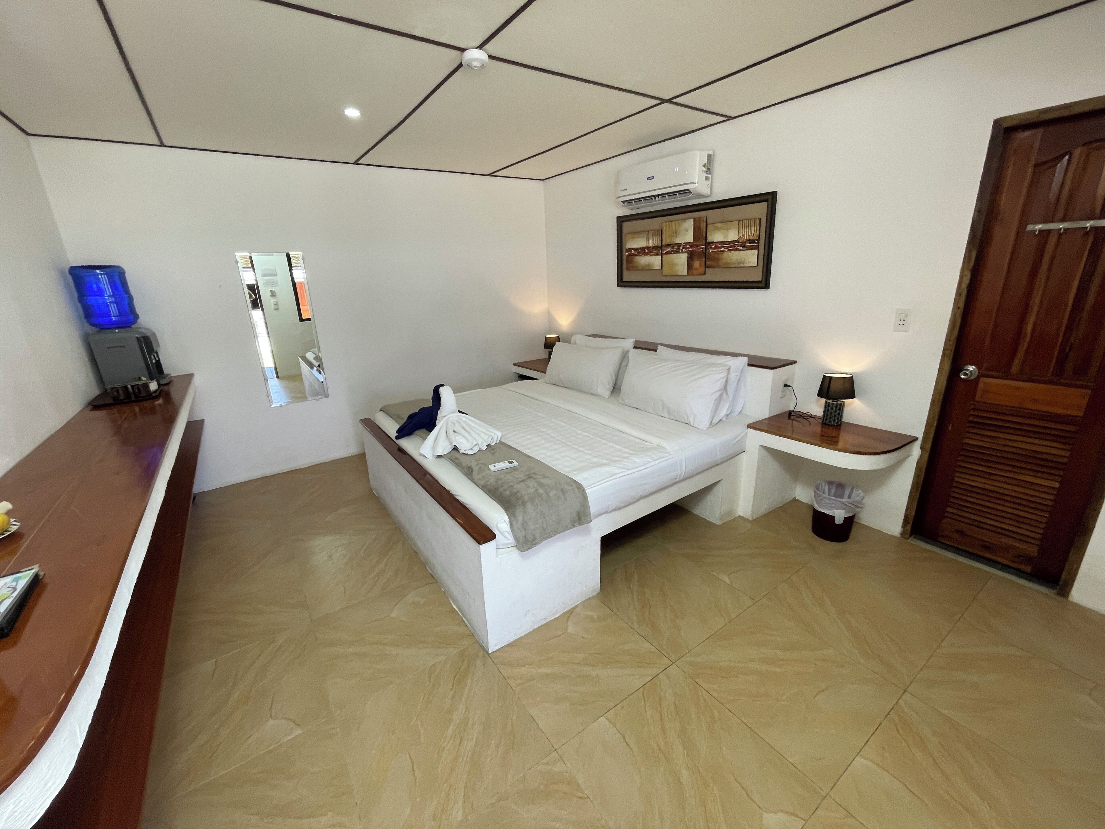A bedroom with a bed, bedside table, and a desk with a water dispenser.