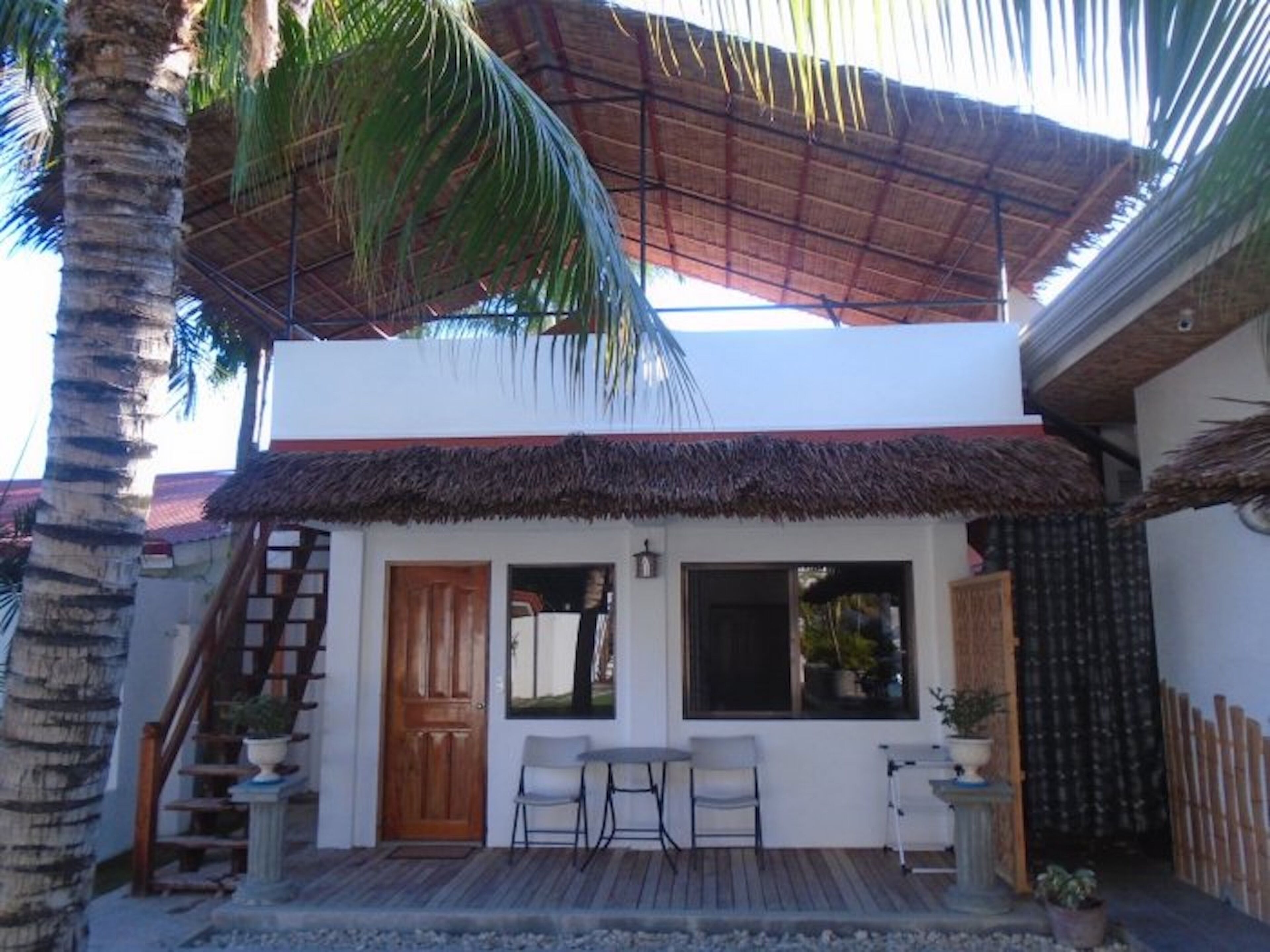 A two-story building with a thatched roof, a wooden staircase, and a small patio area with a table and chairs.