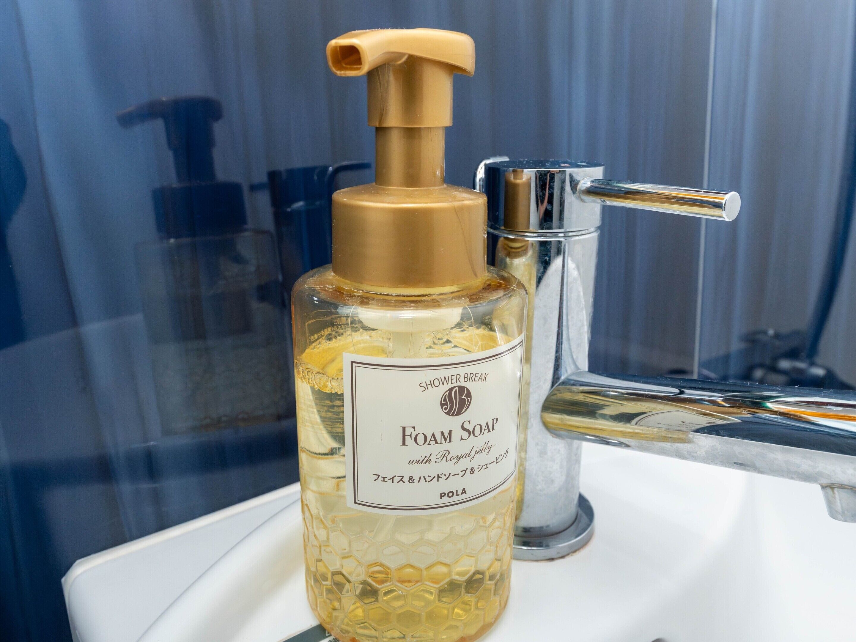 Eine Flasche Schaumbadseife von Shower Break mit Pumpdispenser, platziert auf einer weißen Oberfläche neben einem chromfarbenen Wasserhahn.
