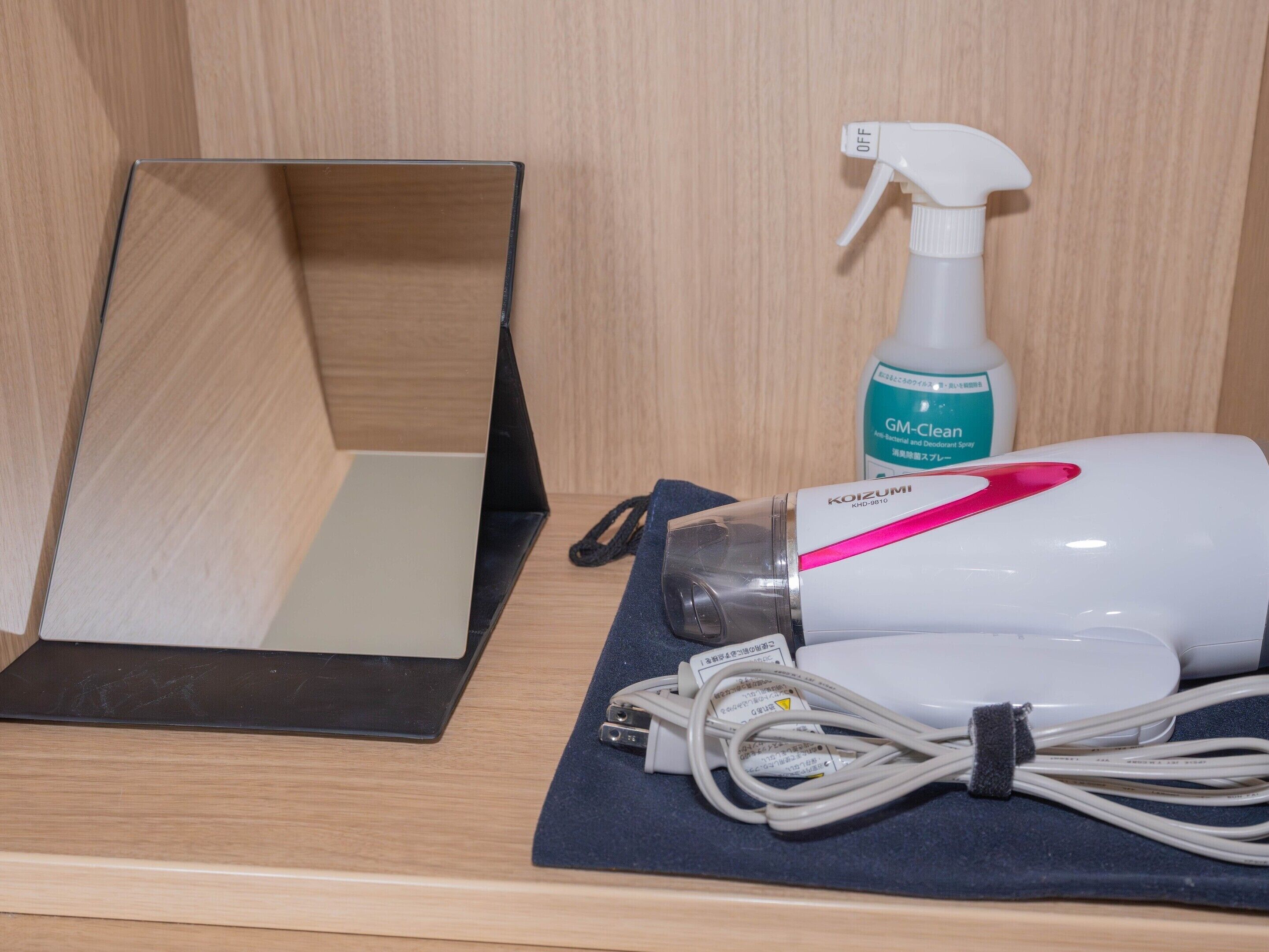 A wooden cabinet with a mirror, a spray bottle, and a hairdryer on a blue cloth.