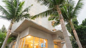 A modern building with large glass windows, palm trees, and a sign indicating a hotel. - The BREAKFAST HOTEL PORTO Ishigakijima (Ishigaki)