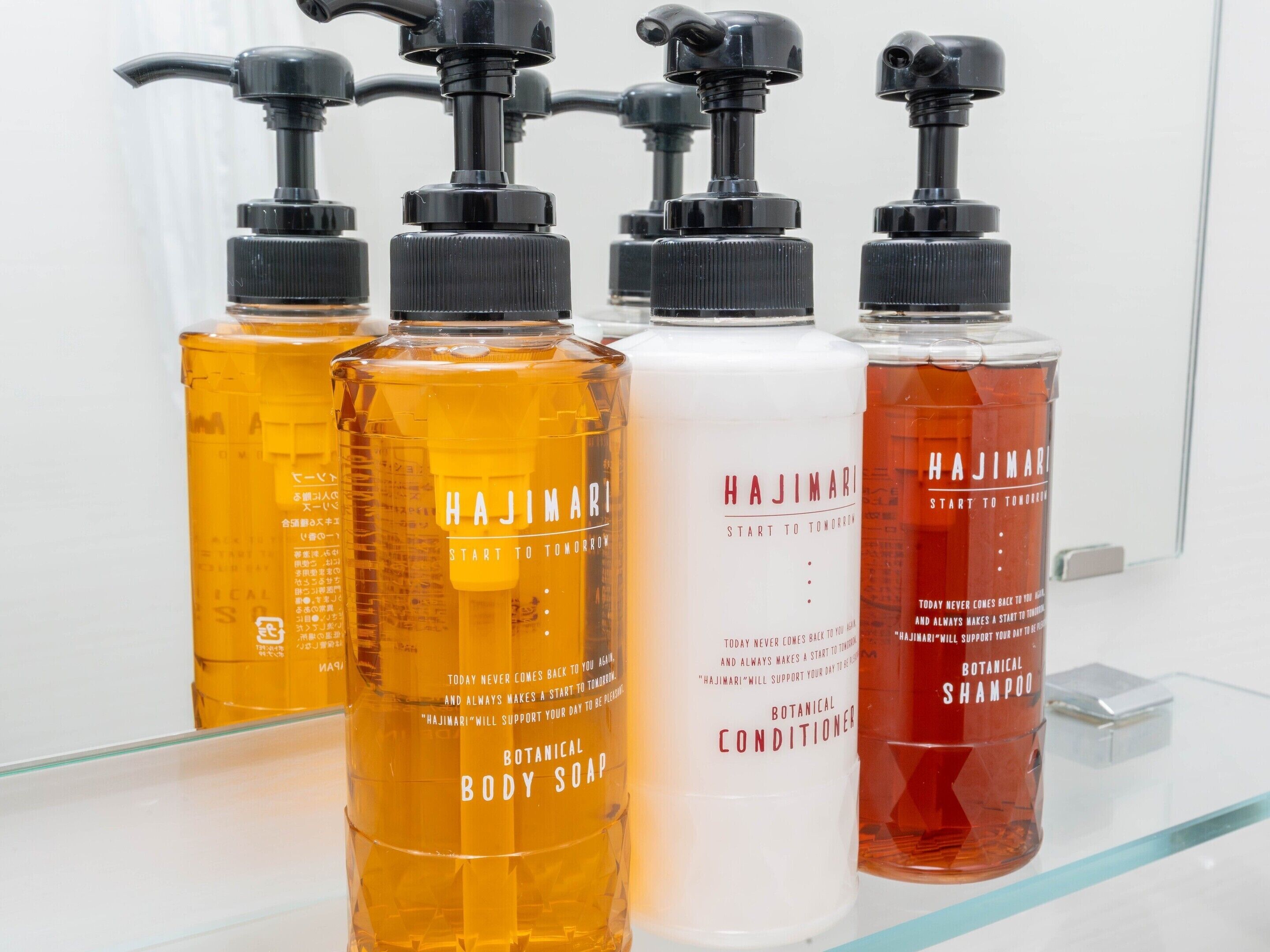 Four bottles of Hajimari body care products on a glass shelf.