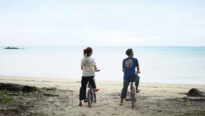 Two people riding bicycles on a sandy beach with the ocean in the background. - The BREAKFAST HOTEL PORTO Ishigakijima (Ishigaki)