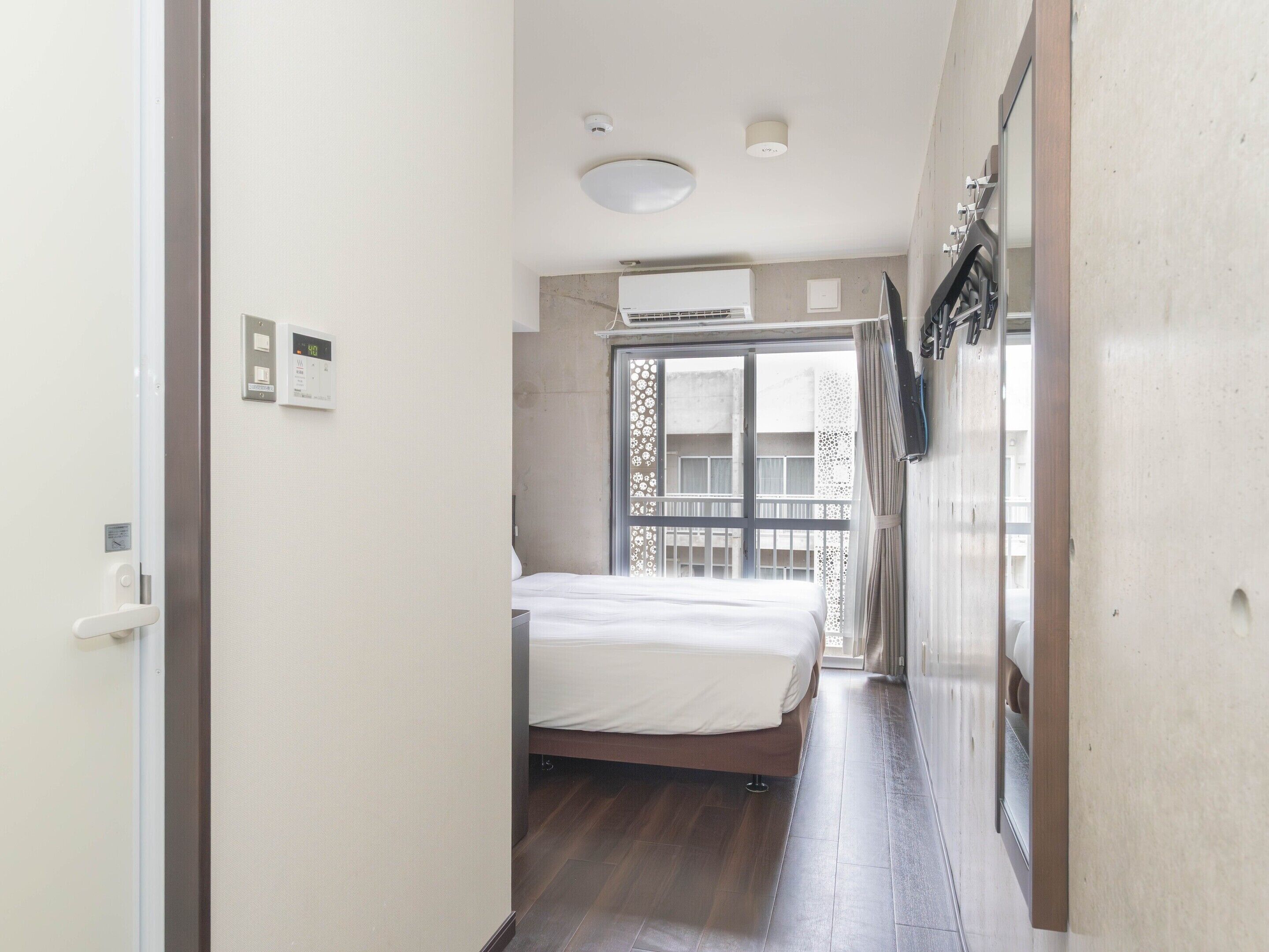Un pasillo estrecho que conduce a un dormitorio con cama, ventana con vistas y una puerta.