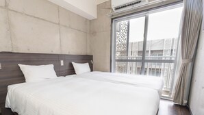 A hotel room with a large bed, a wooden headboard, a window with a view of buildings, and an air conditioning unit. - The BREAKFAST HOTEL PORTO Ishigakijima (Ishigaki)