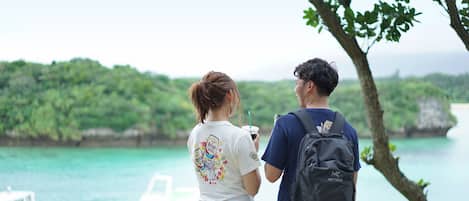 Two people standing by a body of water with boats in the background.