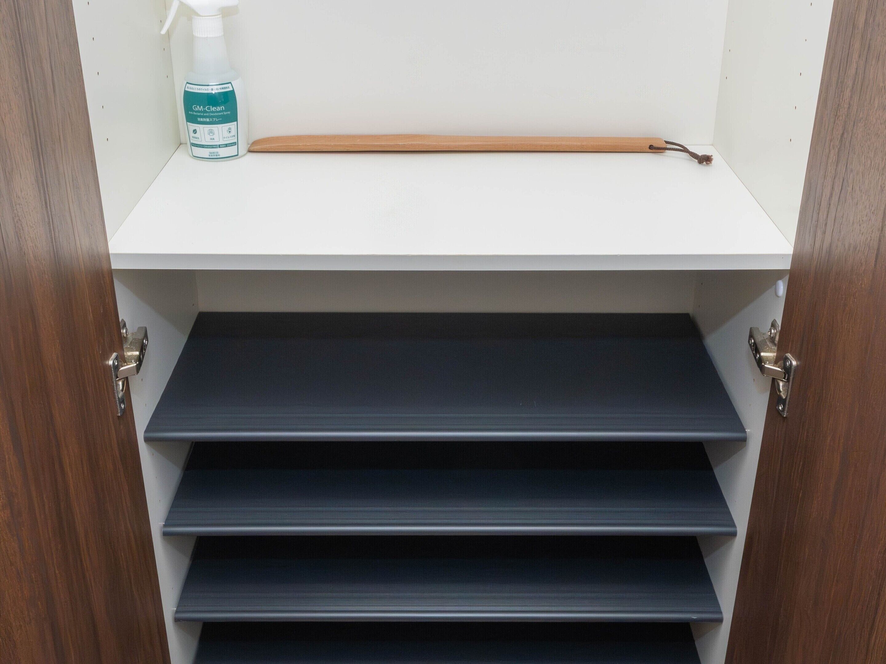 A wooden door with a white interior, a shelf with a bottle, and a wooden stick.