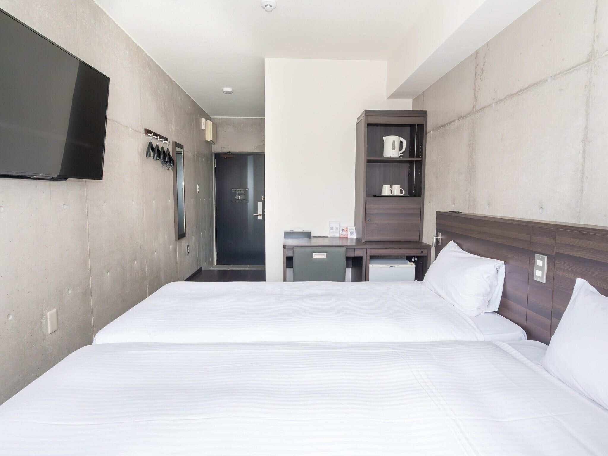 A hotel room with a large bed, a TV mounted on the wall, a coffee machine, and a small desk.