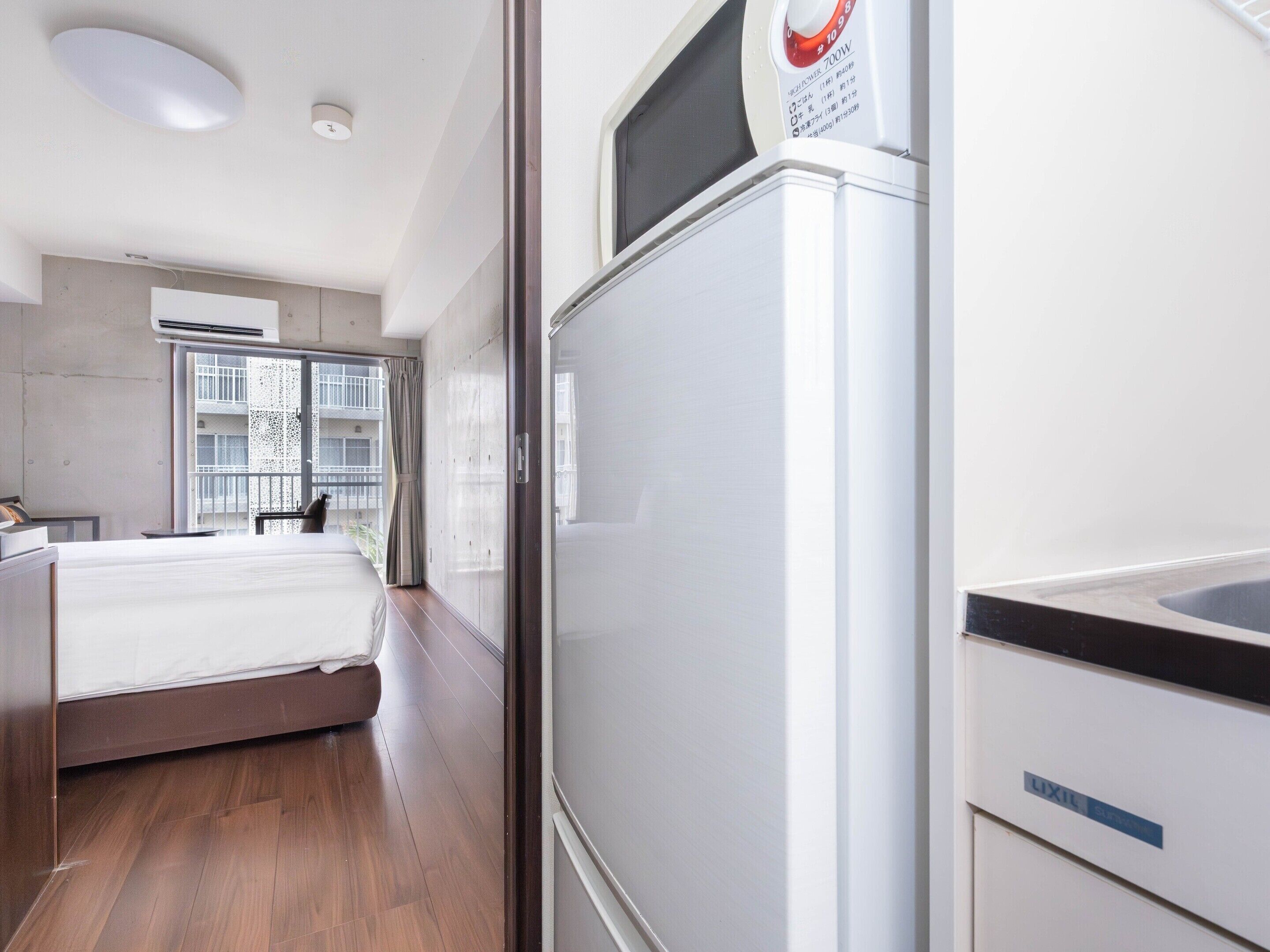 A modern hotel room with a bed, a built-in refrigerator, and a window with a view of the outside.