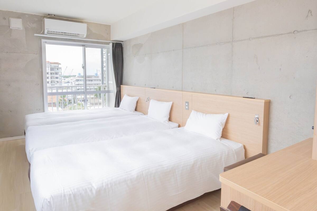 A hotel room with a large bed, a wooden headboard, a window with curtains, and an air conditioning unit.