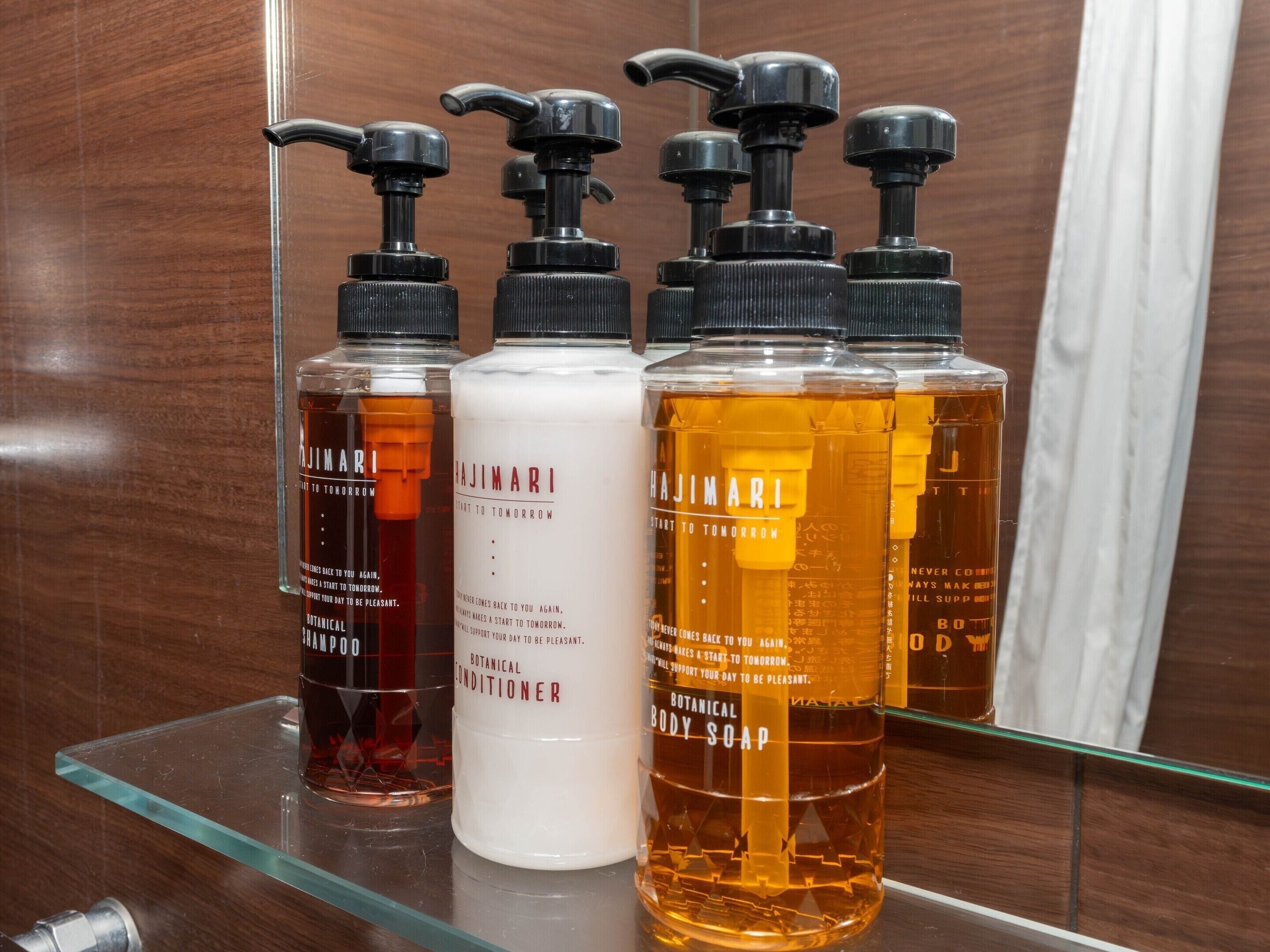 A bathroom with a glass shelf holding four bottles of Hajimari body care products.