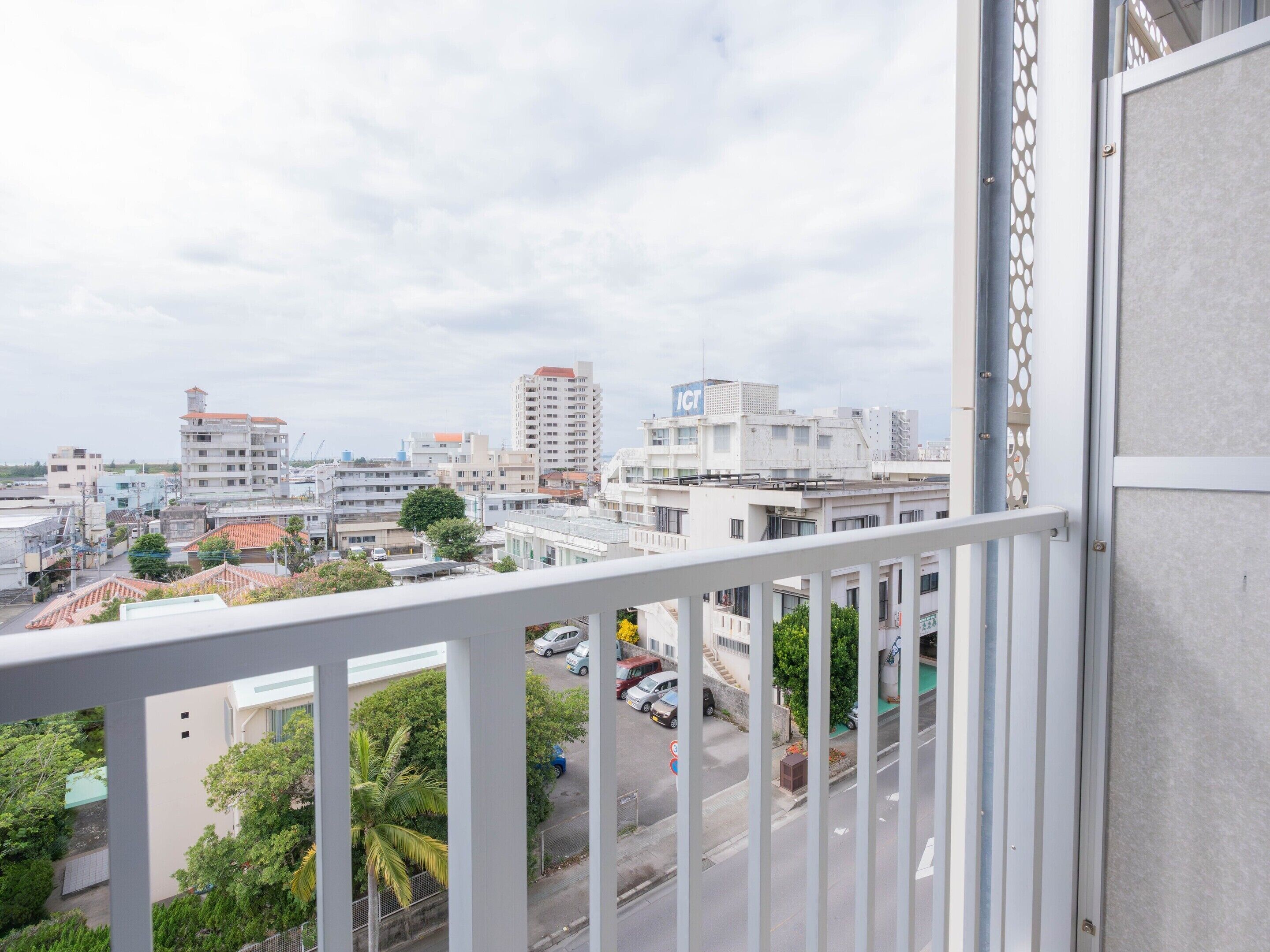 Un balcón con vista a un paisaje urbano, que incluye edificios y coches estacionados.