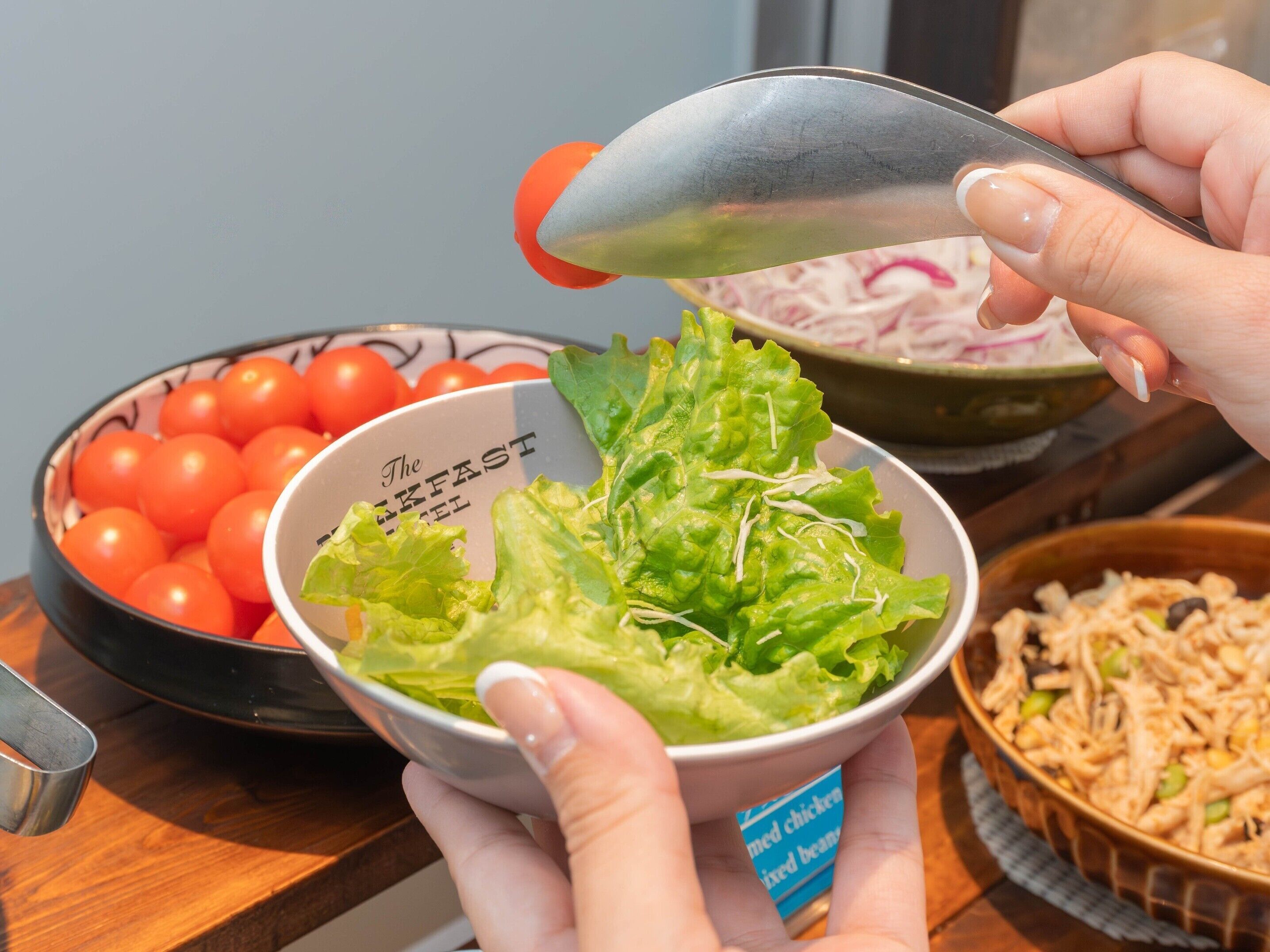 A bowl of salad with lettuce and tomatoes, a bowl of cherry tomatoes, and a bowl of shredded chicken and beans.