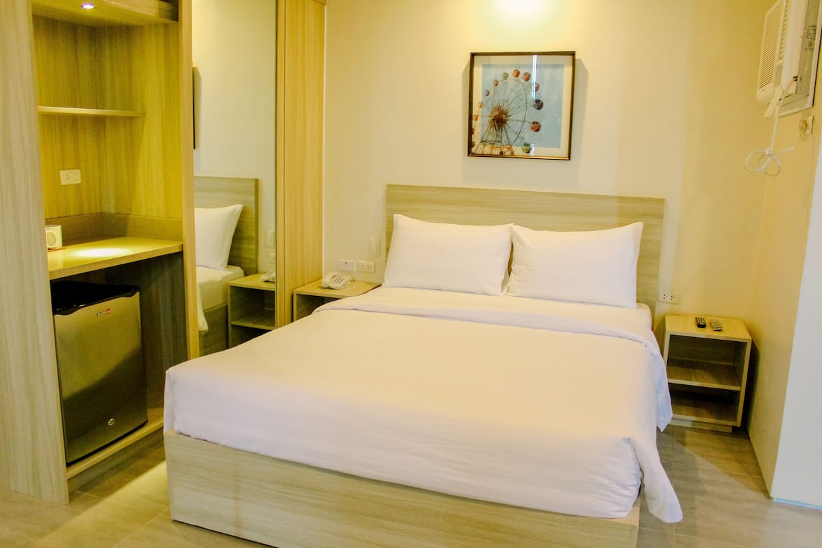 A hotel room with a large bed, a bedside table, a nightstand, a wardrobe, and a mirror.