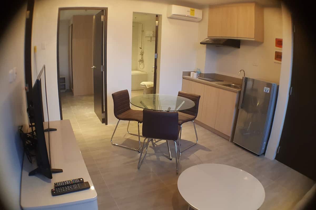 A compact kitchen with a refrigerator, a sink, and a glass-top dining table with four chairs.