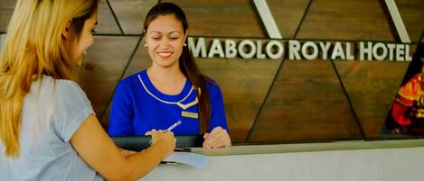 A reception desk at MABOLO ROYAL HOTEL with a wooden wall and a sign.