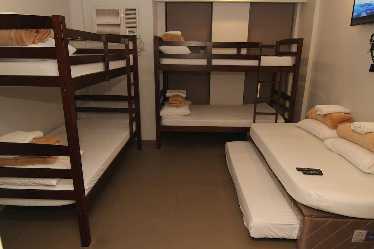 A dormitory room with bunk beds and a single bed. There is a remote control on the single bed.