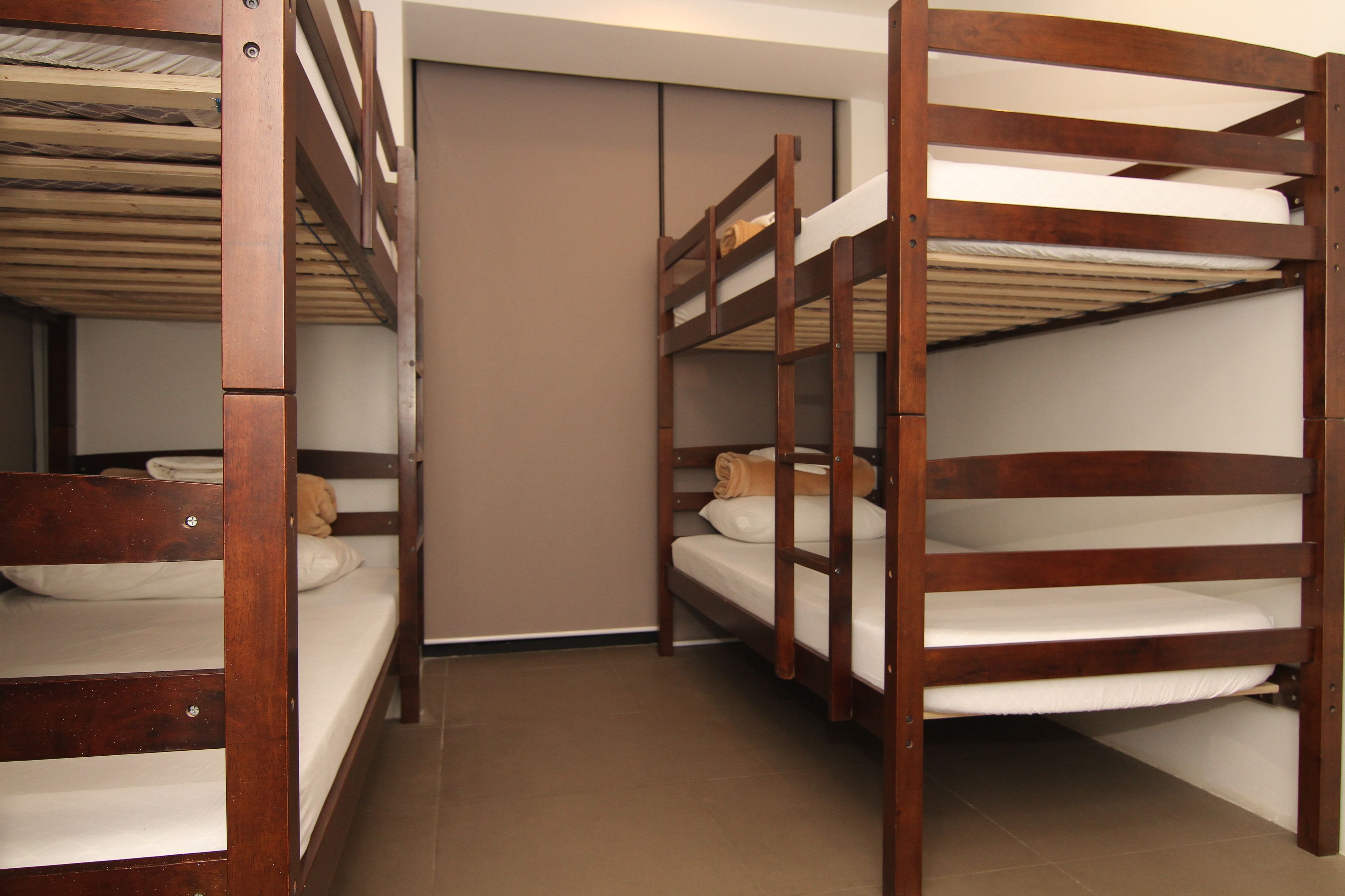 A room with three wooden bunk beds, a closed door, and a tiled floor.