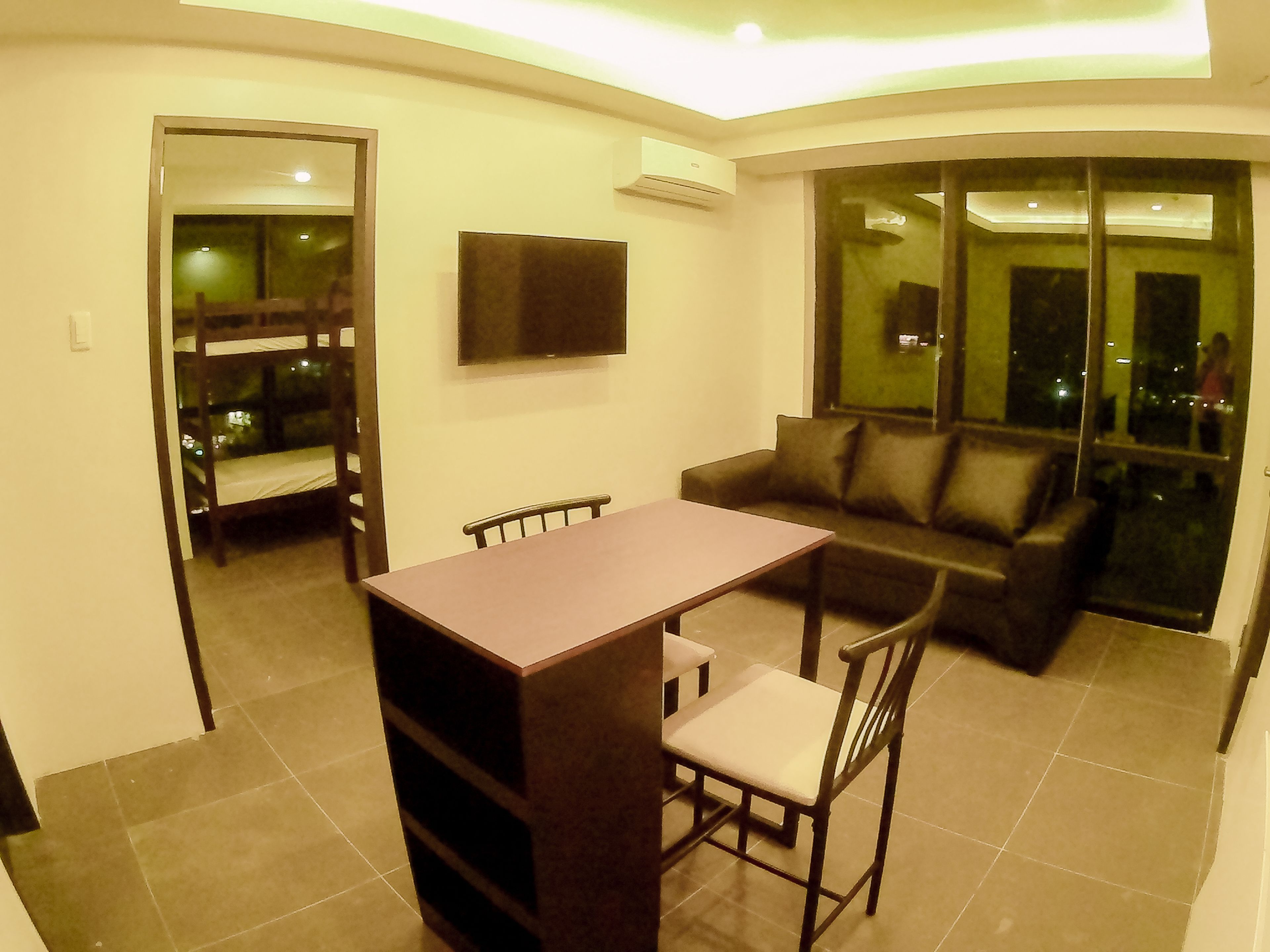 A compact living space with a dining table, a sofa, and a TV mounted on the wall.