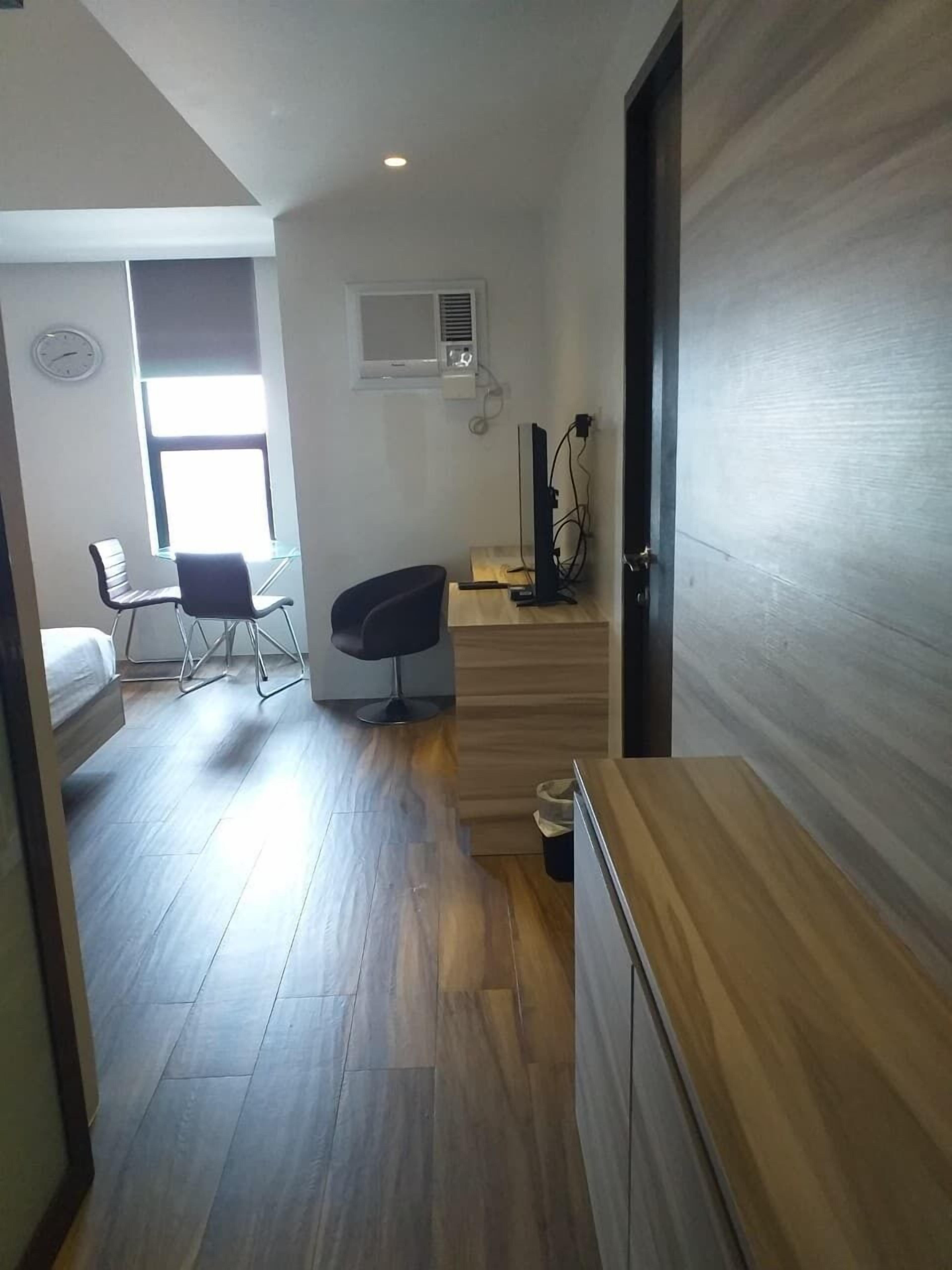 A compact room with a bed, a desk with a computer, a chair, and a window with natural light.