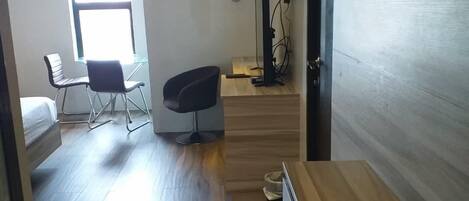 A compact room with a bed, a desk with a computer, a chair, and a window with natural light.