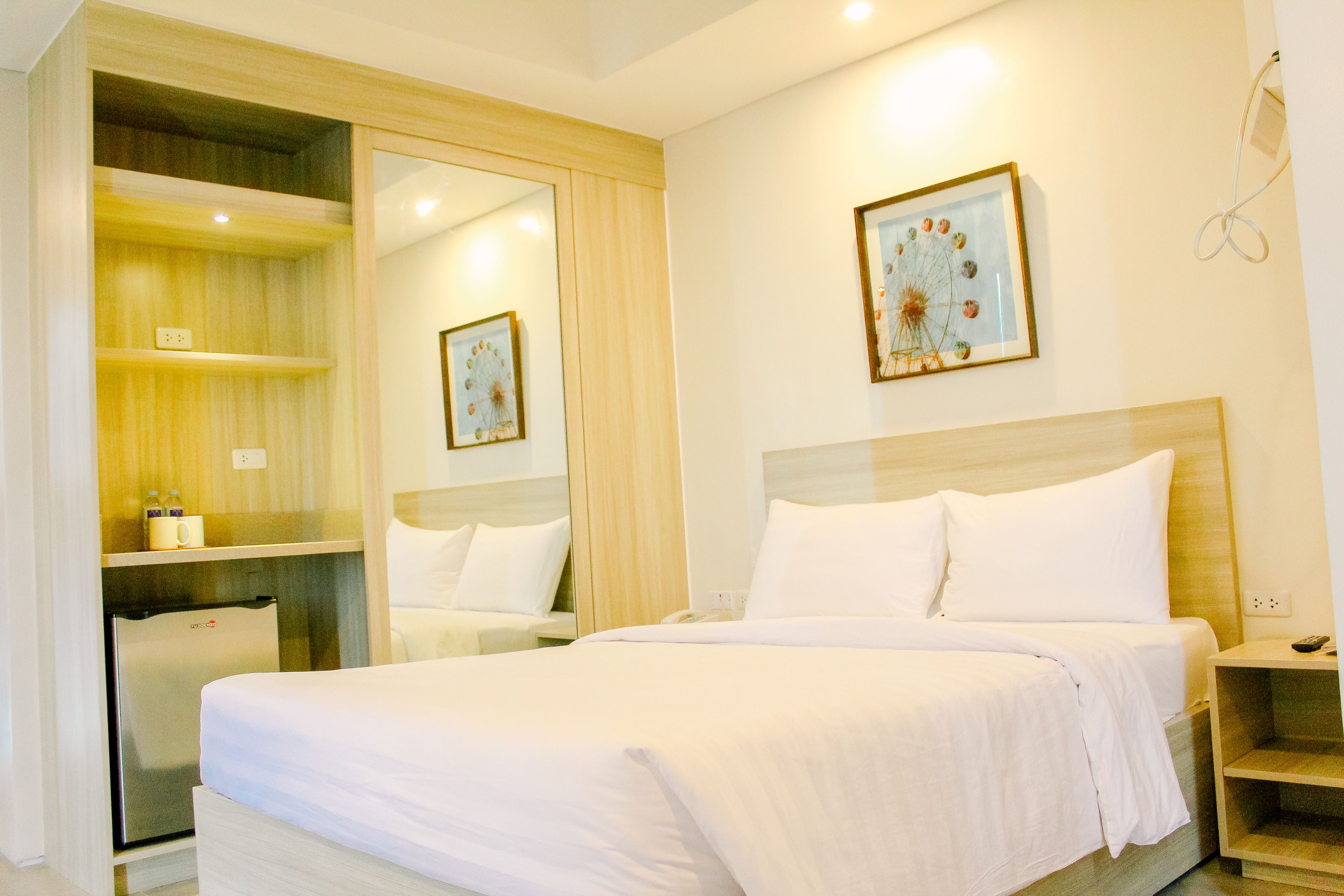 A hotel room with a bed, a small desk, a mirror, and a picture on the wall.