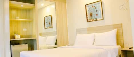 A hotel room with a bed, a small desk, a mirror, and a picture on the wall.