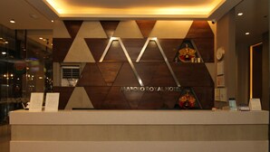 Un mostrador de recepción de hotel con una pared de diseño geométrico y un reloj.