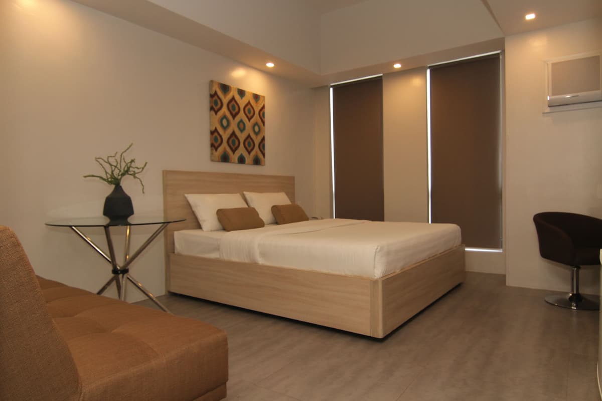 A modern bedroom with a bed, a small table with a vase, a chair, and a wall-mounted TV.