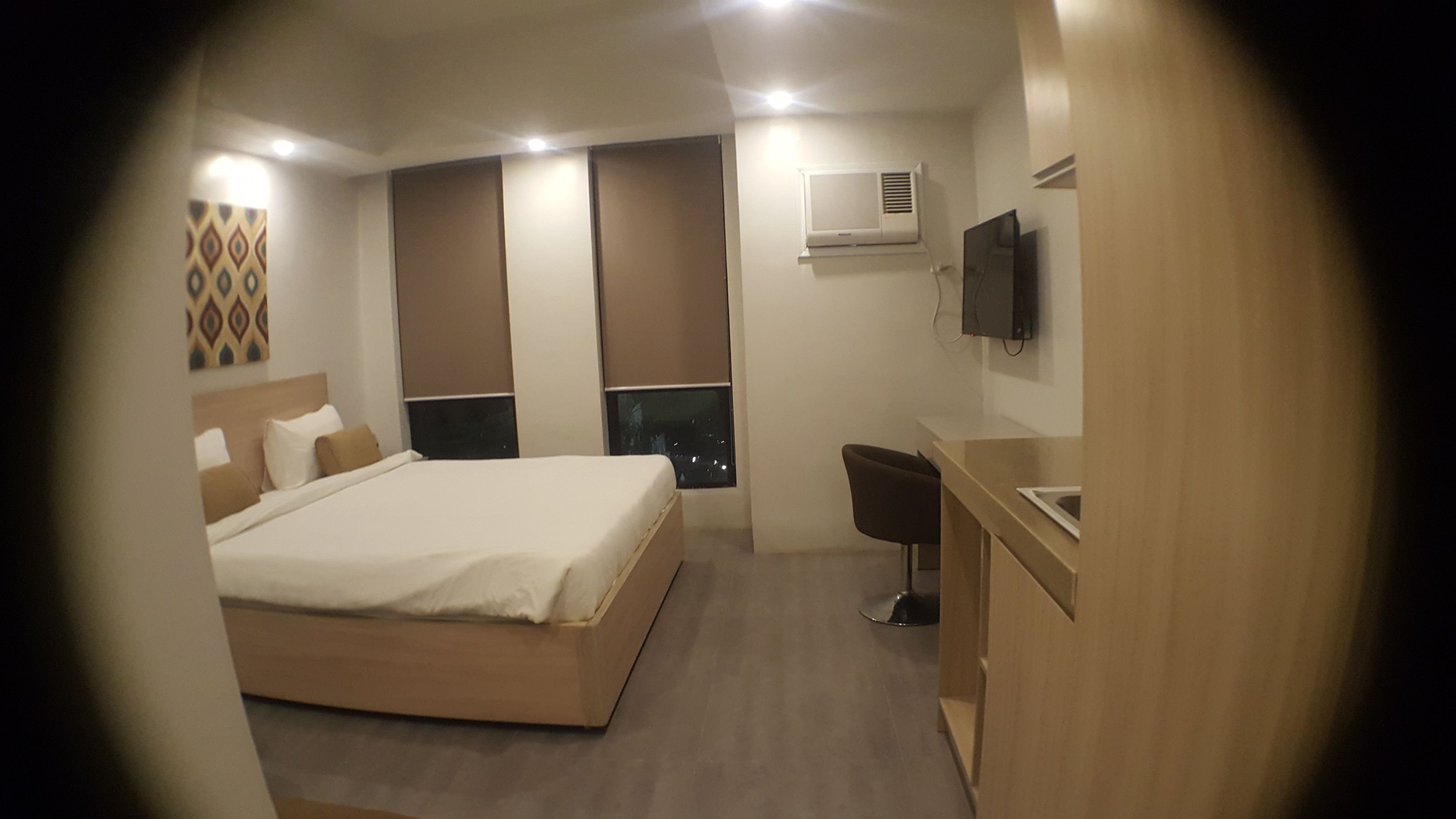 A modern hotel room with a large bed, a desk, and a TV mounted on the wall.