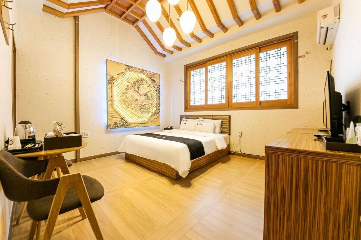 A hotel room with a wooden bed, a desk with a chair, a large window with a grid pattern, and a map artwork on the wall.
