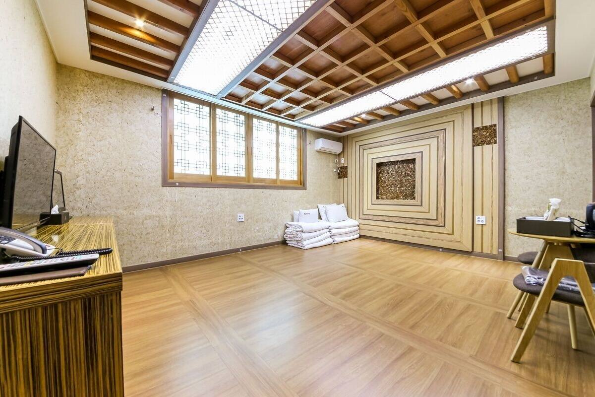 A spacious room with a wooden floor, a reception desk with a telephone, and a large window allowing natural light.