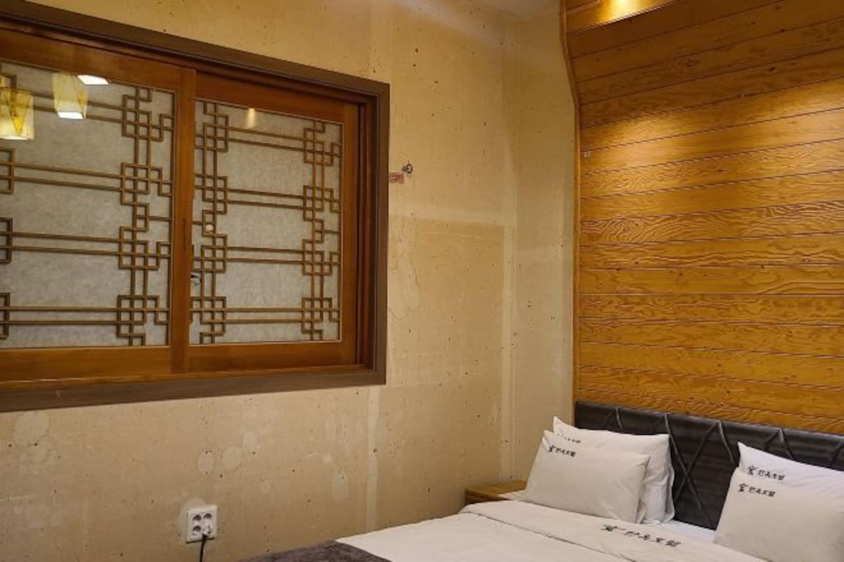 Un dormitorio con cabecera de madera, cama con ropa de cama blanca y ventana con diseño geométrico.