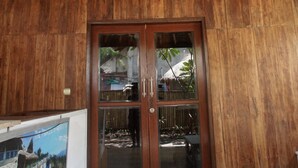 A wooden room with a thatched roof, a wooden door with glass panels, and a framed picture on the wall. - Beach Camp (Gili Trawangan)