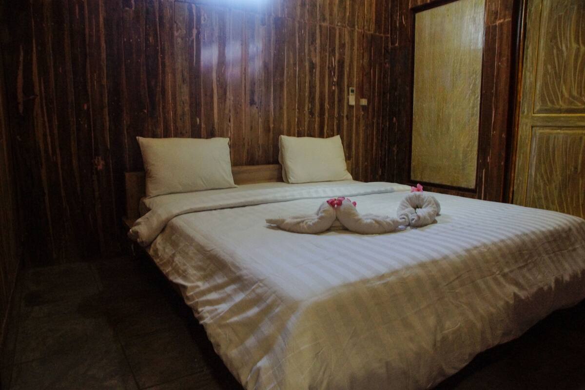 A neatly made bed with pillows and a decorative towel arrangement in a room with wooden paneling.