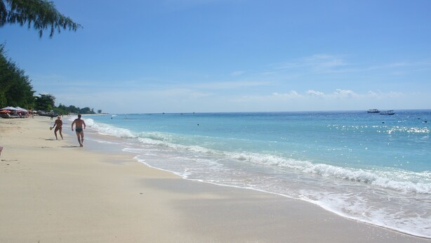 A beach with clear blue water, a sandy shore, and a few people walking. - Beach Camp (Gili Trawangan)