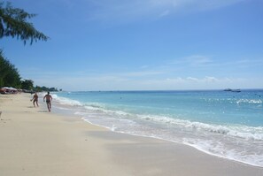 A beach with clear blue water, a sandy shore, and a few people walking. - Beach Camp (Gili Trawangan)