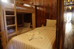 A room with a bunk bed, a single bed, wooden walls, and a visible door leading to another room. - Beach Camp (Gili Trawangan)