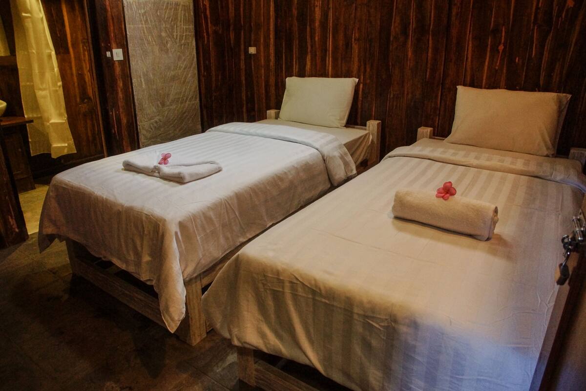 Two single beds with wooden frames and white linens, each with a pillow and a folded towel.