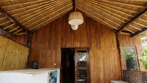 A wooden interior with a thatched roof, a door, and a hanging light fixture. - Beach Camp (Gili Trawangan)