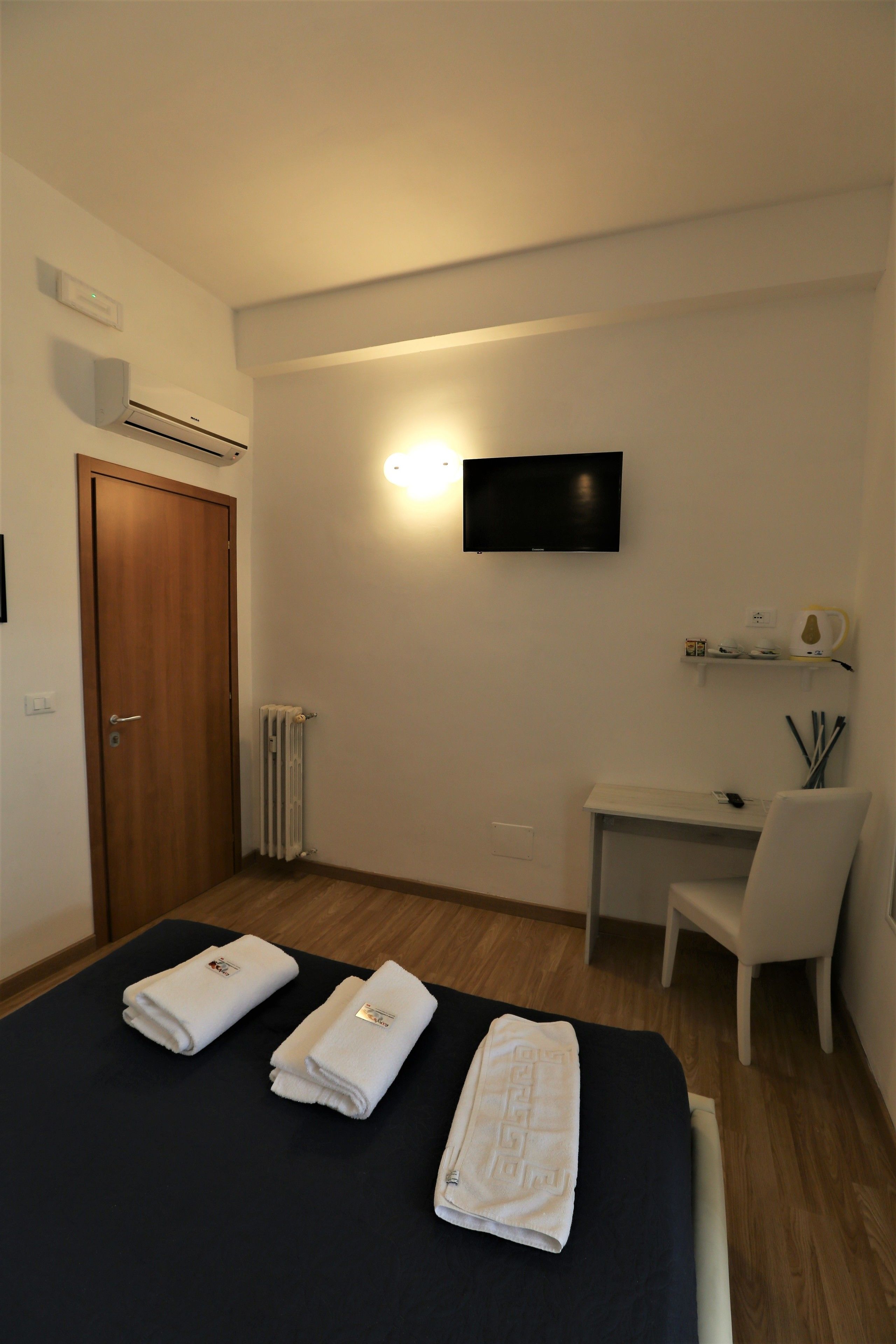A hotel room with a bed, a desk, a chair, a TV, and a radiator.