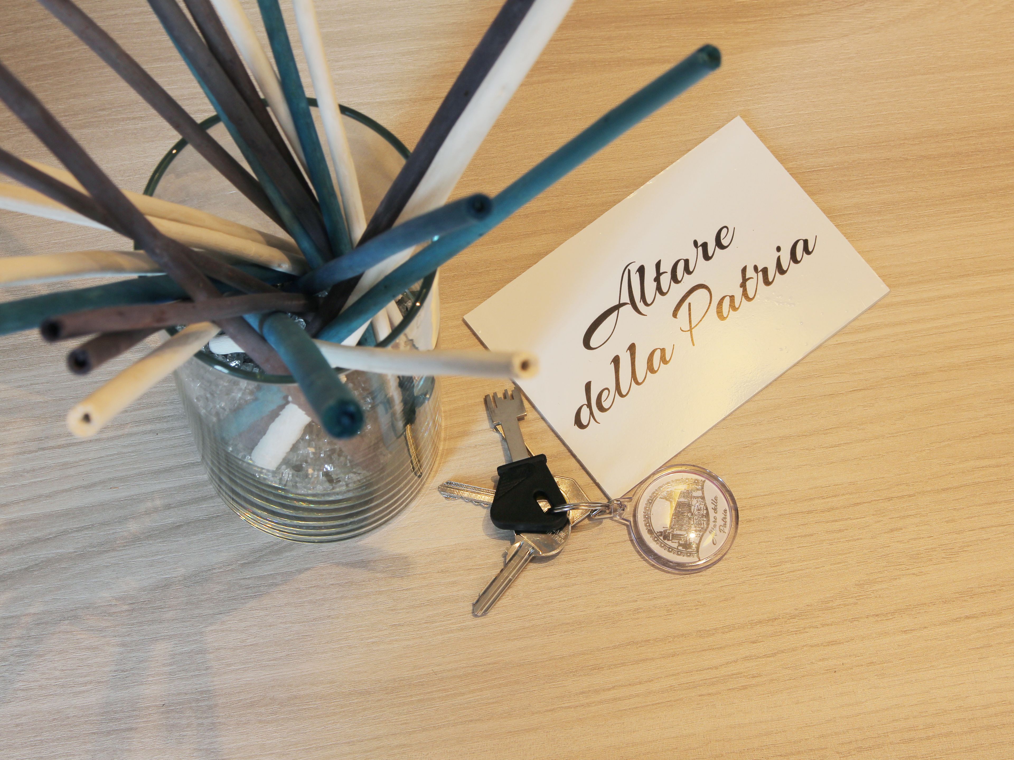 A glass vase with pencils, a card, a keychain, and a key on a wooden surface.