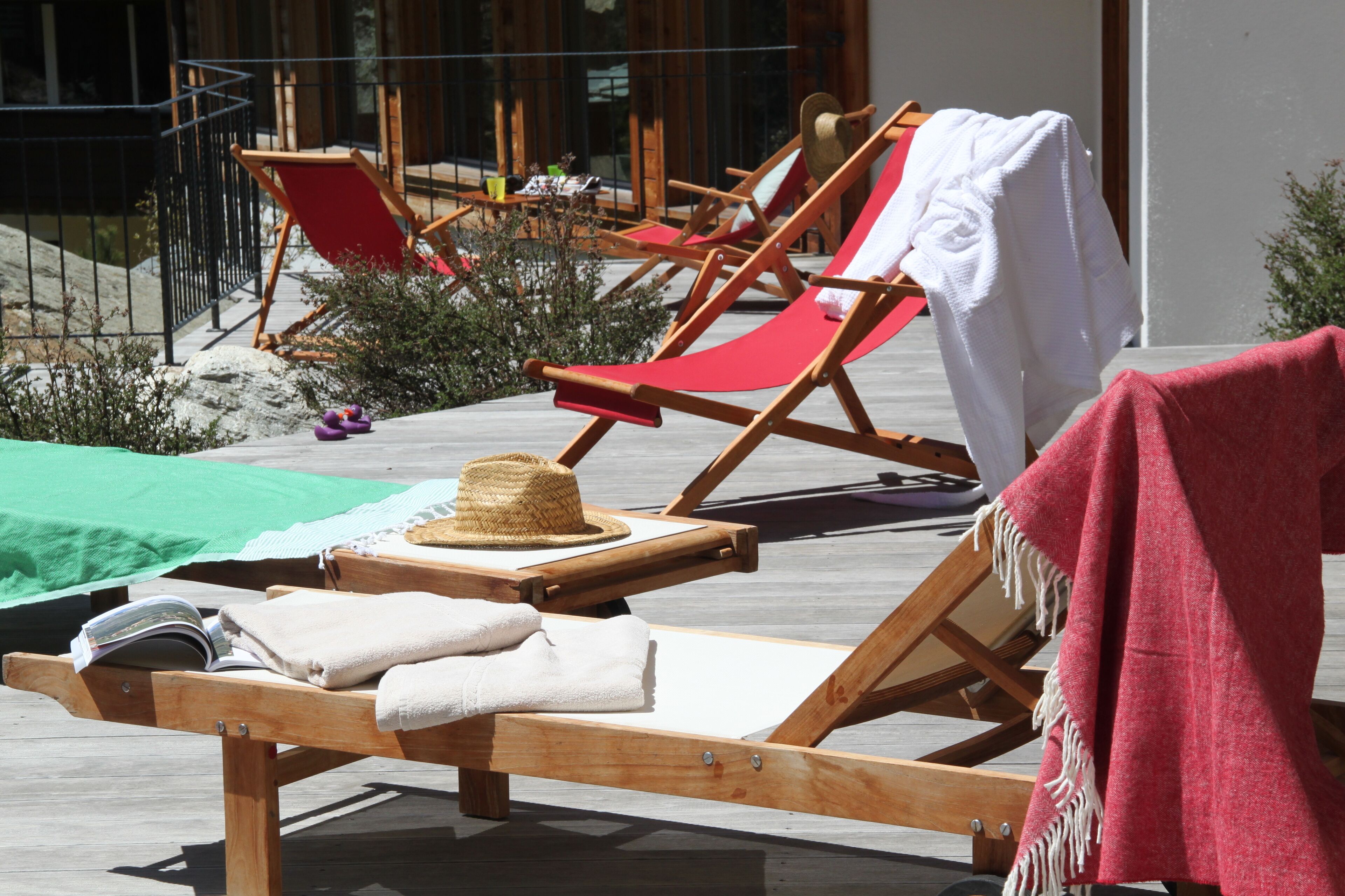 Een houten terras met lounge stoelen, een strohoed en een handdoek op een van de stoelen.