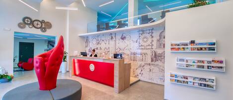 A modern reception area with a red desk, a unique red chair, and a wall with a cityscape mural.