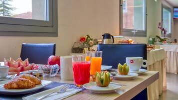 Une table de petit-déjeuner avec des croissants, des fruits, du jus et du café.