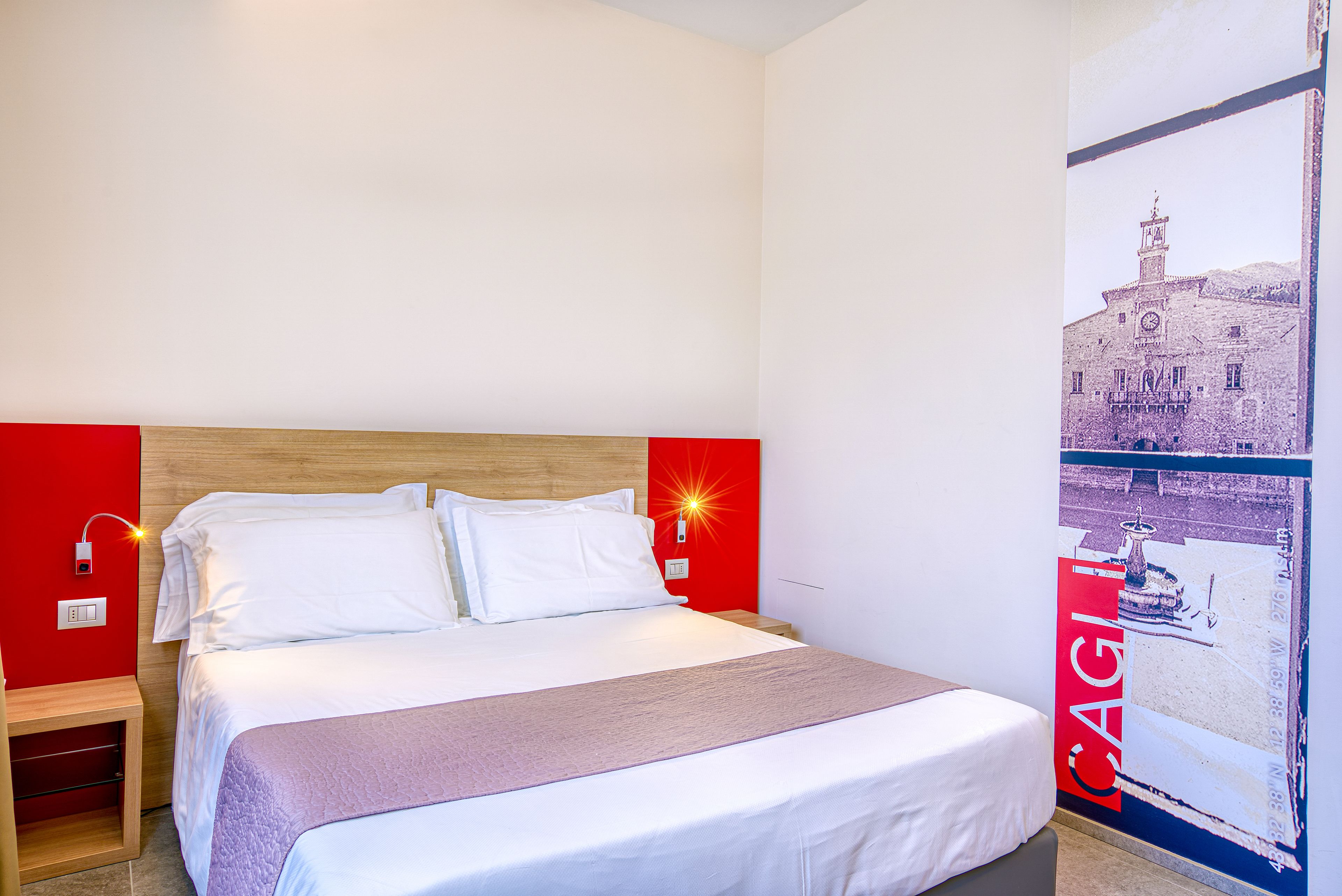 A hotel room with a wooden headboard, white bedding, and a red accent wall.