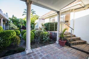 A covered outdoor area with a tiled patio, a staircase, and various plants. - Santorini Guesthouse (East London)