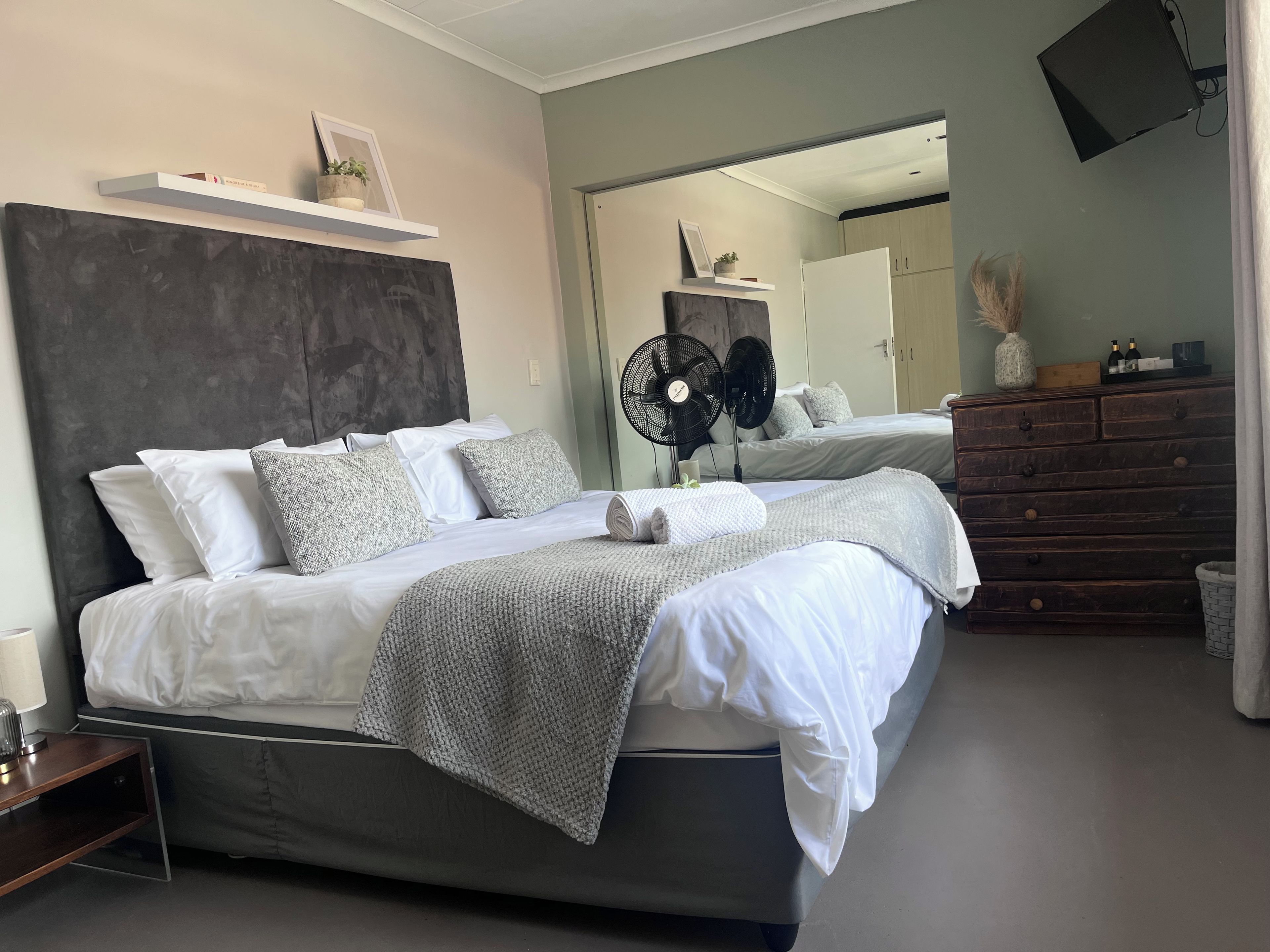 A modern bedroom with a large bed, bedside tables, a dresser, and a wall-mounted fan.